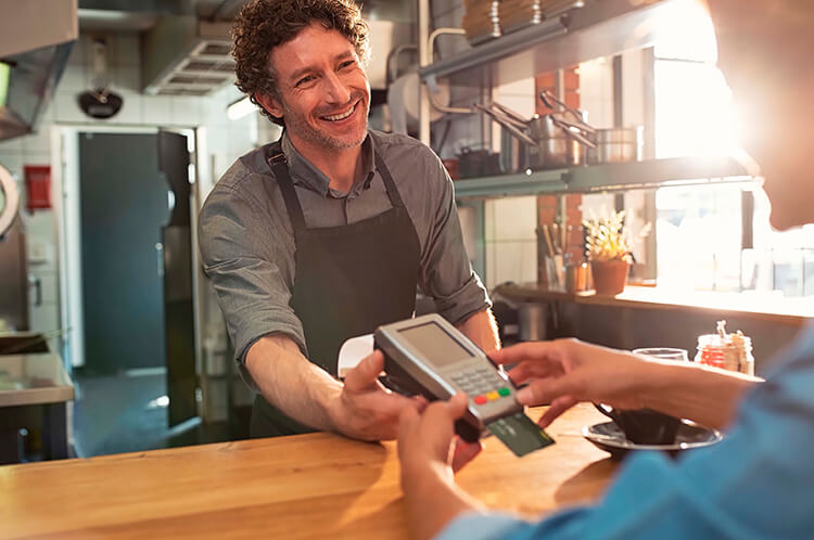 A woman pays for something at a business by using a credit card reader being held out by a man behind the counter.