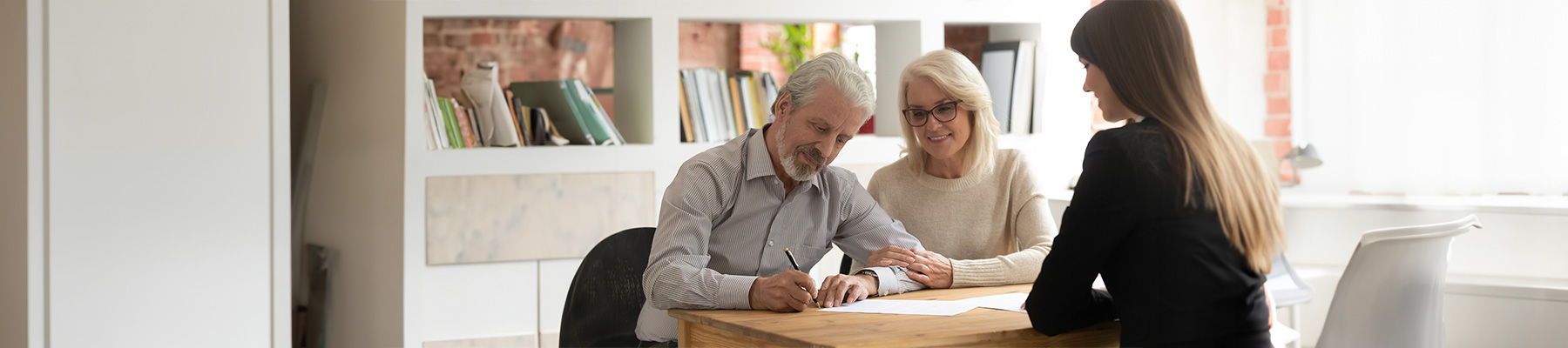 Happy mature clients sign trust papers with bankers.